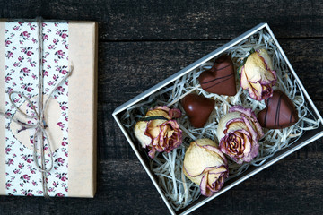 white pink dried roses and gift box with chocolate hearts on wooden table. Valentines Day concept
