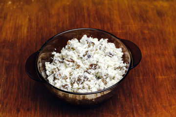 Black glass bowl with cottage cheese and raisins on wooden board.