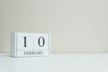 Closeup white wooden calendar with black 10 february word on blurred white wood desk and cream color wallpaper in room textured background with copy space in selective focus at the calendar