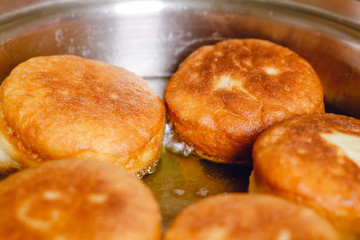 Donuts frying in deep stainless steel pan.