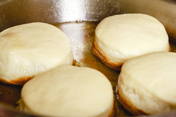 Donuts frying in deep stainless steel pan.