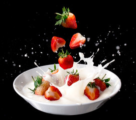 Strawberry falling into splashing milk or yogurt  isolated on black