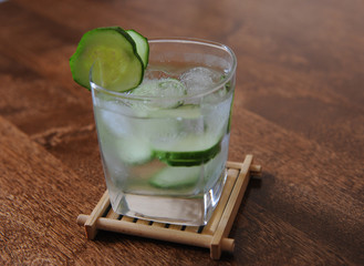 Fresh cucumber summer drink in a glass with ice on wooden table. Free space for text