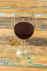 Glass of red wine with autumn leaves on wooden table