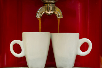 Red espresso machine pours coffee into two cups