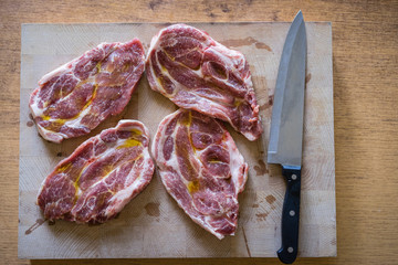 Top view of raw pork chop steaks ready for a grill. Preparing a raw meat by chef knife. Pork chops on a wooden cutting board ready for cooking.