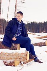 Handsome, stylish and smiling young man in jacket sitting on the woods in the forest. Early spring,...