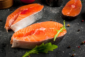 Raw uncooked salmon steaks on a dark gray stone kitchen table. With salt, spices, seasonings, herbs and vegetables for cooking. Close view, copy space