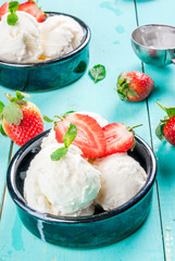     Vanilla ice cream in a classic ice-cream bowls with strawberries and mint, ice cream spoon on light blue wooden table