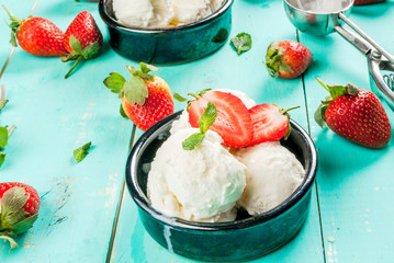     Vanilla ice cream in a classic ice-cream bowls with strawberries and mint, ice cream spoon on light blue wooden table