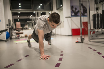 Young man doing push-ups on one hand in the gym
