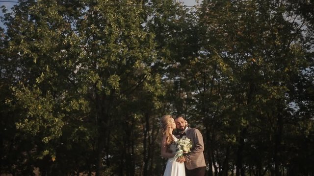 Stylish young beautiful bride and groom kissing in the park