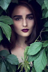 girl in a black hat smiles slightly. girl with red lips and a clock on hand. brunette in black top. beautiful stylish girl with bright makeup. Girl in leaves