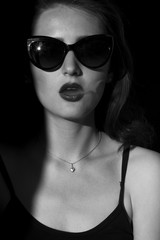 a beautiful girl standing in the shade. Girl in the sun smoking cigarettes and let the smoke out of her mouth. sunglasses. black and white portrait