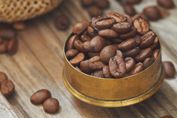 Roasted coffee beans in rustic brass cup on wooden background. Copy space