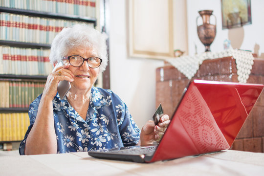 Online shopping, age and technology concept. Senior woman near laptop holding credit card and smartphone.