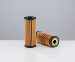 two automotive filter cylindrical shape of orange color on a white background with reflection