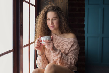 Pretty girl on a windowsill with cup in her hands