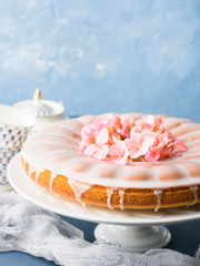 Obraz na płótnie Canvas Bundt ring cake with sugar frosting decorated with pink flowers. Spring summer elegant breakfast set. Easter mother day festive treat. Selective focus