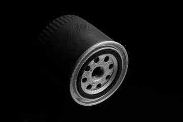 metallic automotive filter cylindrical shape with drops of water on a black background close up