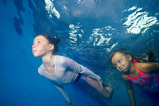 Two little girls swim underwater in the pool on a blue background. Portrait. The view from under the water. Horizontal orientation