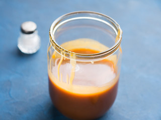 Home made salted caramel in glass jar on dark blue background. Copy space