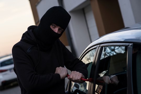 Auto thief in black balaclava trying to break into car