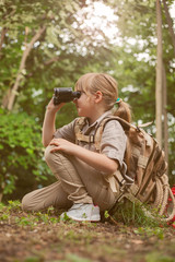 young girl scout, explores  nature with binoculars on camping tr