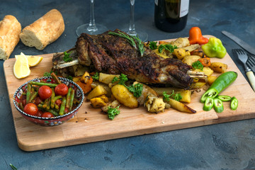 Roast shoulder of lamb on baked potato and carrots, wooden board, top view