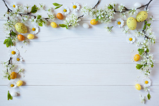 Easter white wooden background with flowering branches cherry plum, daisies and yellow eggs
