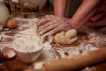 Fototapeta premium Senior woman hands knead dough on table in home kitchen
