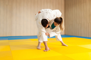 Young female judoka trying to throw larger and stronger male opponent