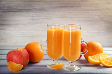 Glasses of fresh pumpkin smoothie with apples and oranges on wooden table