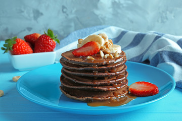 Blue plate with delicious chocolate pancakes decorated with strawberry and banana on wooden table