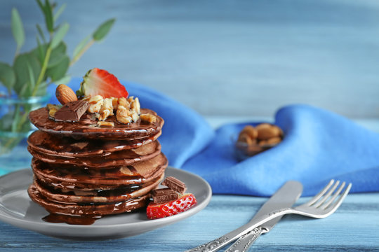 Plate with delicious chocolate pancakes decorated with strawberry and nuts on wooden table