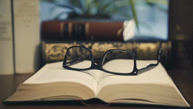 old books on desktop with modern glasses on open pages - vintage film style, smooth tracking shot