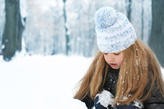 Cute little girl playing with snow in winter park