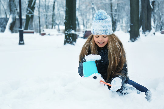 Cute little girl making snowman in winter park
