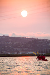 Kayaks on water as sun sets over wetland, marina, and hillsides covered with homes in California
