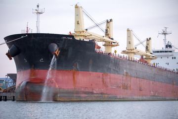 Large commercial ship sits at dock while pumping water out of a port