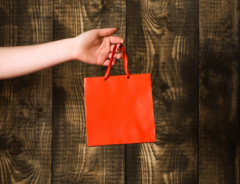 red orange shopping bag in female hand on wooden background