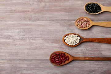 Assortment of haricot beans in spoons on wooden background