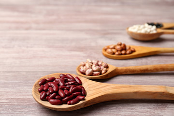 Assortment of haricot beans in spoons on wooden background