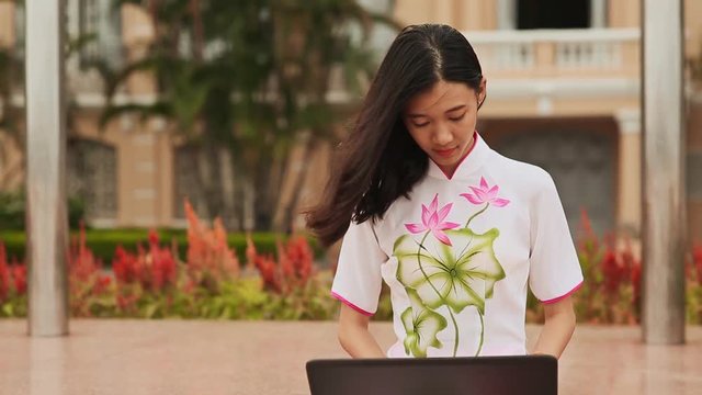 Pretty Asian girl sitting with a laptop in the park in national dress Ao Dai