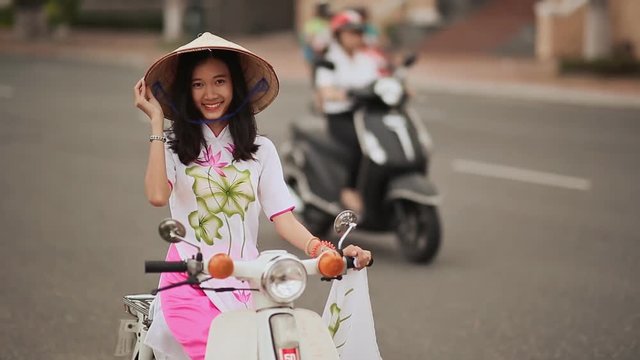 Beautiful girl in national dress Ao Dai and Non La cap sits on a motorbike