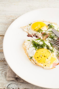 fried eggs with bacon on a white plate on a wooden table