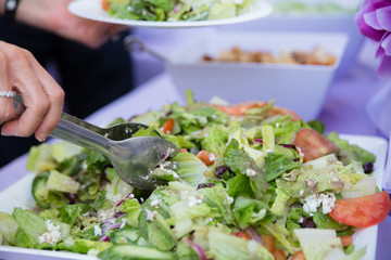 Person serves up a plate of salad on a purple table cloth at a party - 135515800