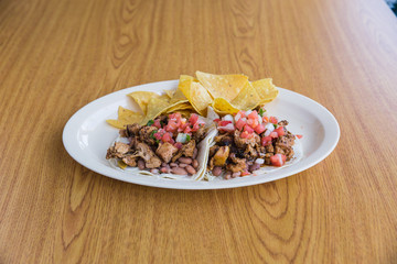 Seasoned chicken tacos with chips and salsa on white plate on wooden table