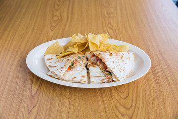 Chicken quesadilla with chips on white plate on wooden table