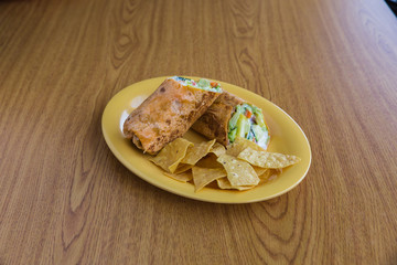 Caesar roll with side of chips on yellow plate on wooden table